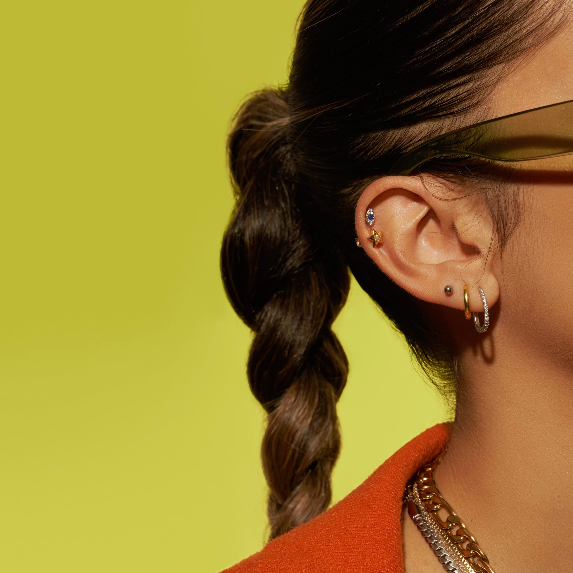 green background with model showing off her ear stack. orange shirt, braided hair. APT. 144 Jewelry Studio